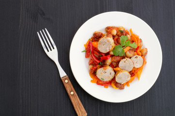 Stewed beans with vegetables and sausages. on black background.