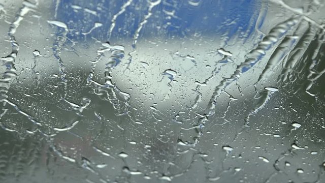 Driving on a rural German road in heavy rain without windscreen wipers. Focus on the windscreen to make rain more visible while defocusing the landscape and road.