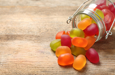 Glass jar and scattered jelly candies on wooden table, space for text