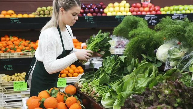 Young female seller standing near greens and vegetables on the supermarket