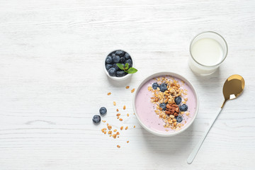 Bowl of tasty oatmeal with blueberries and yogurt on white wooden table, flat lay. Space for text