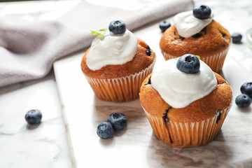 Marble board with tasty muffins, cream and blueberries on table