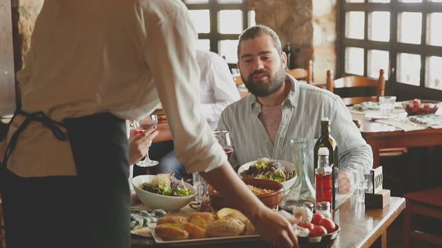 Beautiful couple eating out at a restaurant while young and obliging waitress is serving them dishes