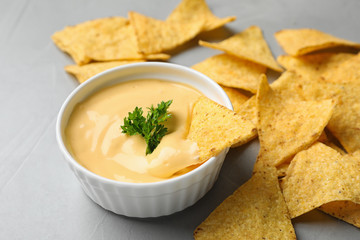 Tasty cheese sauce with Mexican nachos chips on grey table, closeup