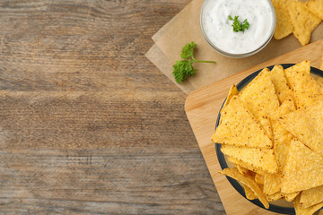 Mexican nacho chips with sauce on wooden background, flat lay. Space for text