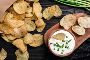 Sour cream in and chips on black wooden table, flat lay