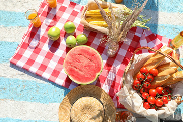 Straw hat and different products for summer picnic on checkered blanket, flat lay