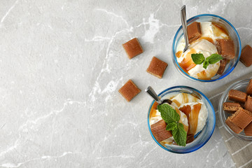 Glasses of delicious ice cream with caramel sauce, candies and mint on light grey marble table, flat lay. Space for text