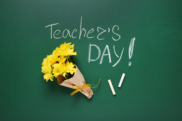 Flat lay composition with flowers and inscription TEACHER'S DAY on green chalkboard