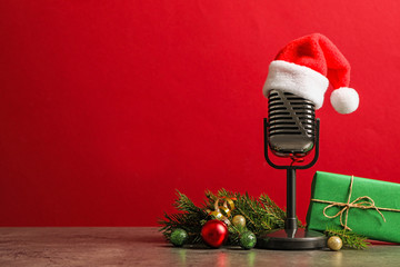Microphone with Santa hat and decorations on grey table against red background, space for text....