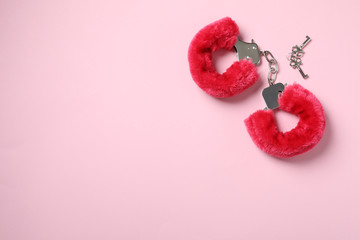 Red furry handcuffs and keys on pink background, top view with space for text. Sex toy