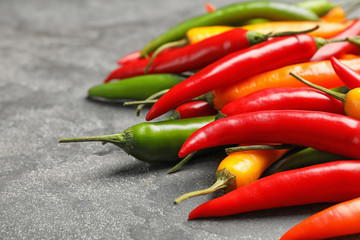 Different ripe chili peppers on grey table, closeup