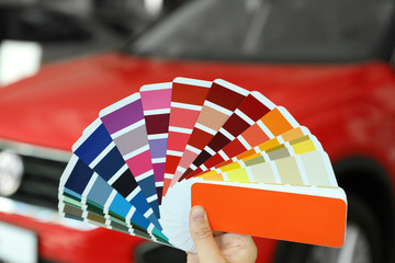 Young woman holding palette with color samples at car service station, closeup