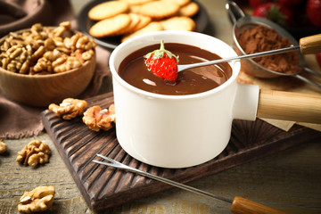 Dipping strawberry into fondue pot with milk chocolate on wooden table