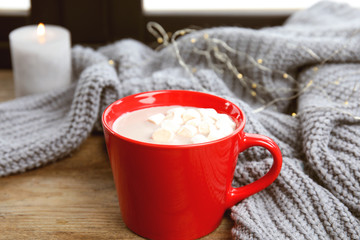 Cup of hot cocoa with marshmallows and sweater on window sill. Winter drink