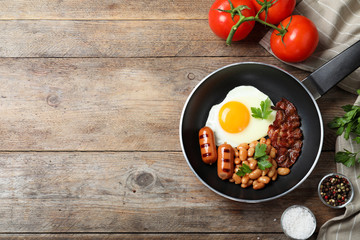 Frying pan with traditional English breakfast on wooden table, flat lay. Space for text