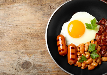 Frying pan with traditional English breakfast on wooden table, top view. Space for text
