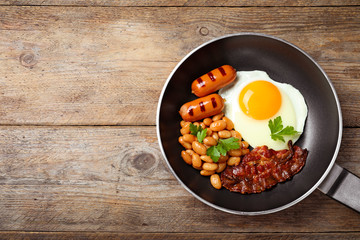 Frying pan with traditional English breakfast on wooden table, top view. Space for text
