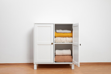 Wooden cabinet with clothes near white wall. Stylish furniture for wardrobe room