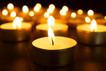 Burning candles on table in darkness, closeup. Funeral symbol