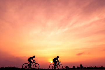Silhouette of cyclists ride bicycle on sunset background. Two men Ride on bike on the road, Sport and active life concept