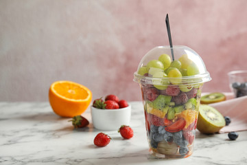 Fresh tasty fruit salad in plastic cup on white marble table. Space for text