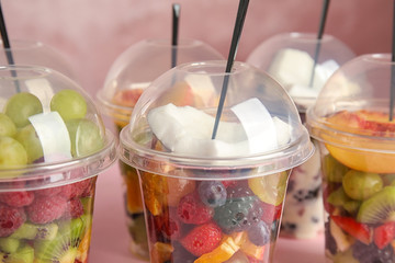 Fresh tasty fruit salad in plastic cups on pink background, closeup