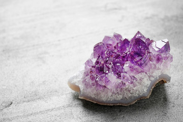 Beautiful purple amethyst gemstone on grey table, space for text