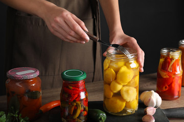 Woman taking pickled pattypan squash from jar at wooden table, closeup