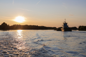 Naklejka premium A barge moved across big river at sunset, dark and slow