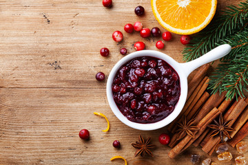 Cranberry sauce in ceramic saucepan with ingredients for cooking decorated with fir tree for Christmas or Thanksgiving day on rustic kitchen table. Top view.
