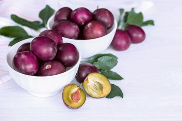 ripe plum. purple plums in white cups on white background. plums and plum halves closeup.
