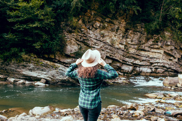 Woman raised hands enjoying landscape  in mountains  Young girl in a hat