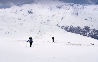 Two climbers ascending Rampsgill Head in the snow in winter from the summit of The Knott near Hartsop in the Lake District