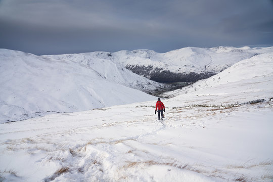 A hiker walking through fresh snow while descending from The Knott towards Hayeswater Gill near Hartsop in the Lake District.