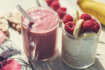 Banana, raspberry, oatmeal and yogurt smoothie and ingredients in two glass cups