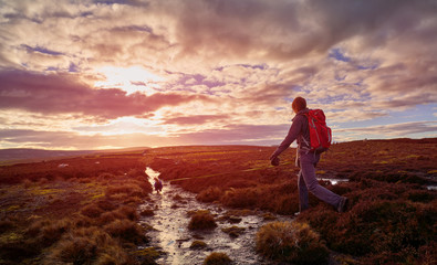 Strong red sky sunset with a hiker walking along a narrow trail across Edmundbyers Common with their dog.