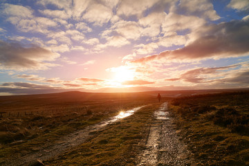 The sun setting over Bolts Law with vibrant orange and red tones to the ground and sky as a hiker walks off into the distance.