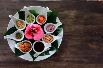 Miang kham or miang kam is a traditional Southeast Asian snack from Thailand. with Lotus petals.white disc on the old table.