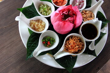Miang kham or miang kam is a traditional Southeast Asian snack from Thailand. with Lotus petals.white disc on the old table.