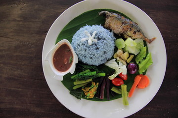 Thai Food - Rice butterfly pea with Fried mackerel and vegetable in white disc on the old wooden. Top View.