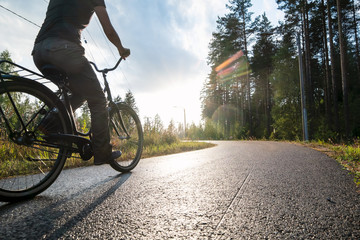 Fototapeta na wymiar A woman rides a bike on a bicycle path in the rain on a summer evening in the sunshine next to a pine forest. Healthy lifestyle concept.