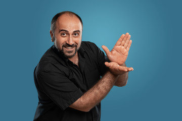 Naklejka premium Close-up portrait of a brunet middle-aged man with beard, dressed in a black t-shirt and posing against a blue background.