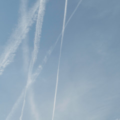 Five chemtrails in the air on one half of the image and copy space, in the blue sky, on the other half of the image.