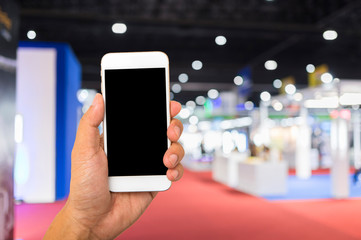 Hand hold blank smartphone on blue exhibition hall background