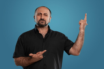Fototapeta premium Close-up portrait of a brunet middle-aged man with beard, dressed in a black t-shirt and posing against a blue background.