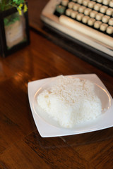 Jasmine rice was shaped in star put on a white plate placed on a dark brown wooden table. there are an artificial flower and typewriter in the background