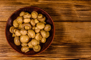 Ceramic plate with canned mushrooms on wooden table. Top view