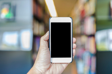 Hand hold blank smart phone on blur book in library background
