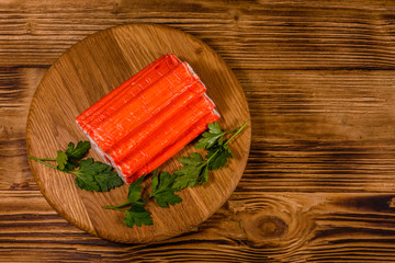 Cutting board with pile of crab sticks and parsley twig on a wooden table. Top view